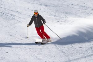 Skier in red gear enjoying a downhill run on a sunny winter day.